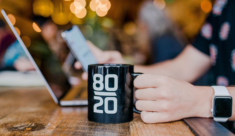 person working on a computer with an 80 20 mug