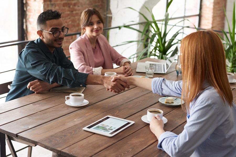 A couple shaking hands with someone across a table.