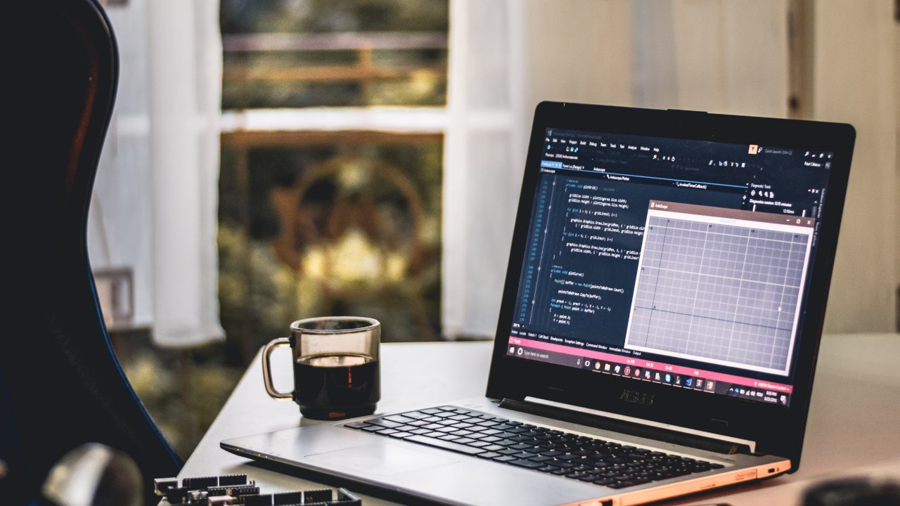 computer open on desk next to phone and coffee