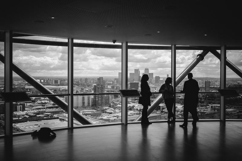 black and white photo of 3 business people with their backs to floor to ceiling windows