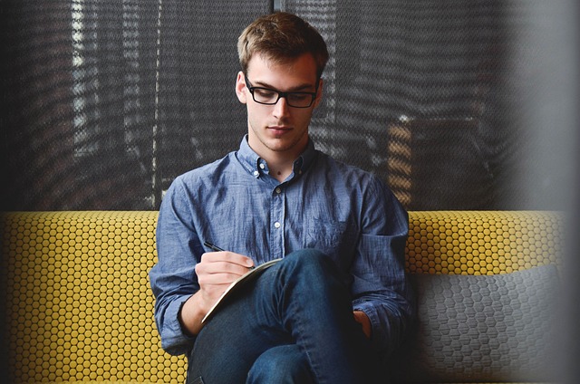 young entrepreneur in glasses sitting on a couch writing in a notebook