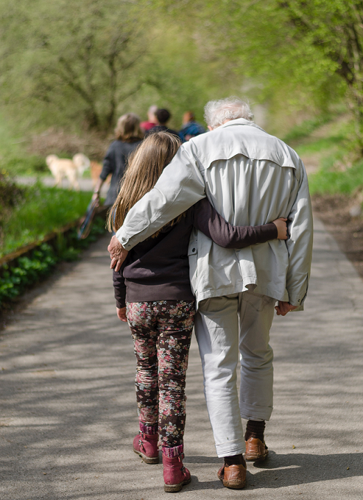 granddaughter with arm wrapped around her grandfather walking along a path.